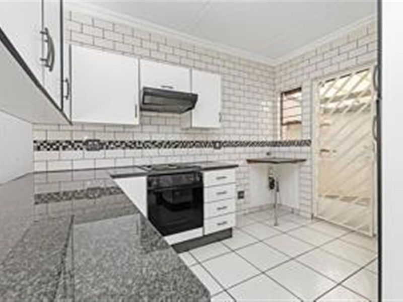 A clean, functional kitchen featuring granite countertops, subway tile backsplash, built-in oven with extractor fan, and ample cabinetry with direct access to an exterior area.