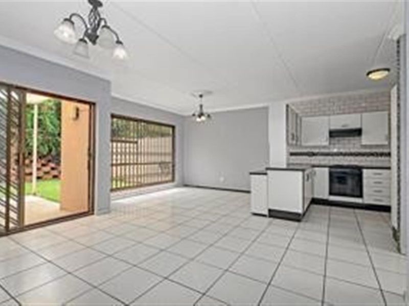 Spacious open-plan living and kitchen area featuring tiled floors, modern cabinetry, built-in appliances, and direct access to an outdoor patio area.