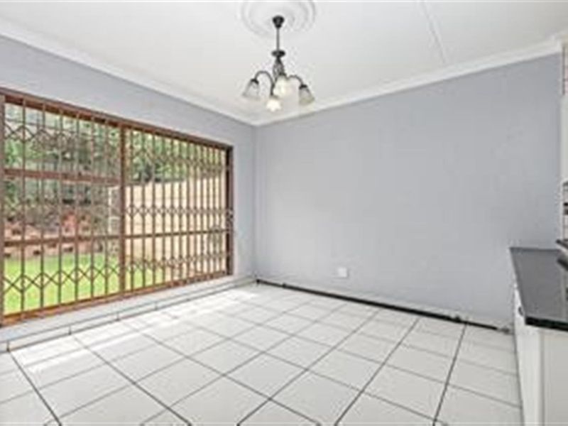An empty open-plan living and kitchen area featuring tiled flooring, a security gate on the sliding door, and a decorative ceiling rose.