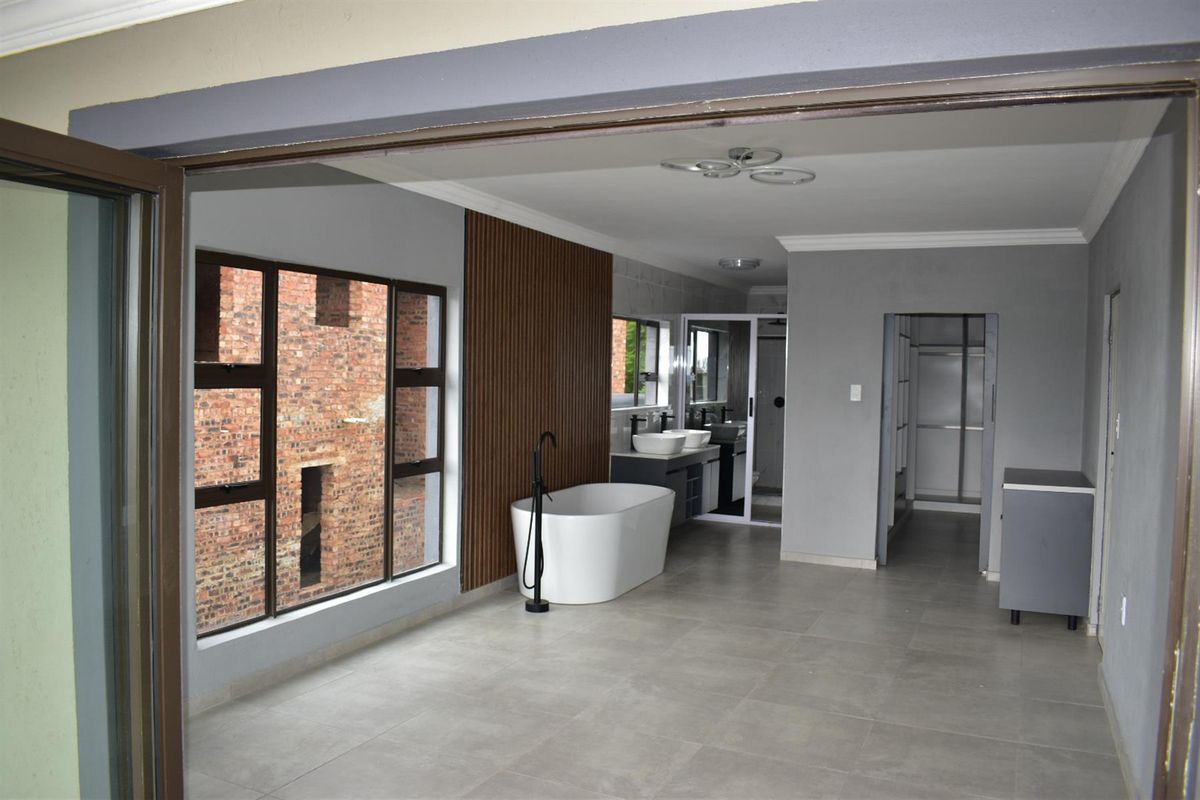 Modern open-plan bathroom featuring a freestanding bathtub, double vanity with vessel sinks, and contemporary wood-slat wall paneling.