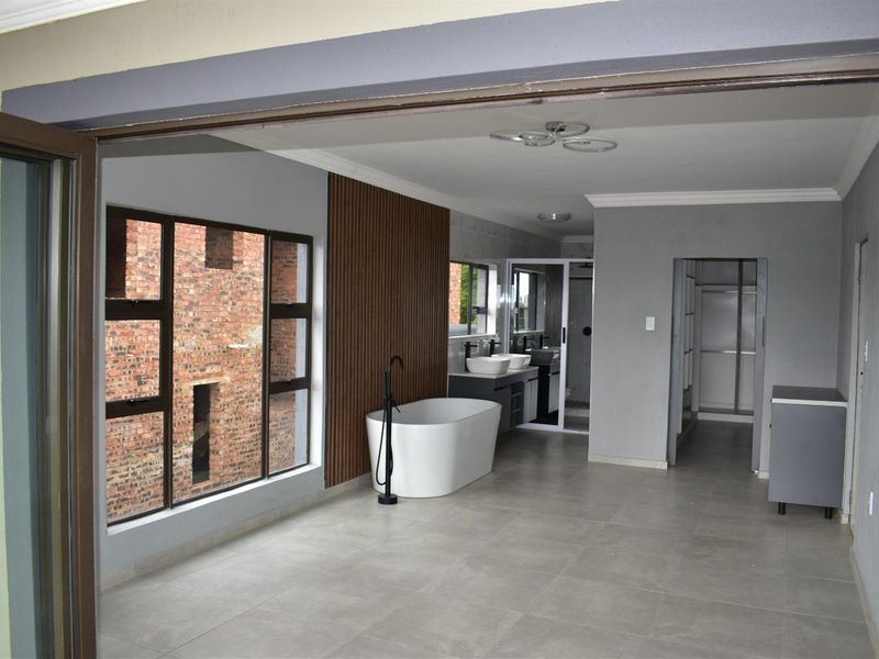Modern open-plan bathroom featuring a freestanding bathtub, double vanity with vessel sinks, and contemporary wood-slat wall paneling.