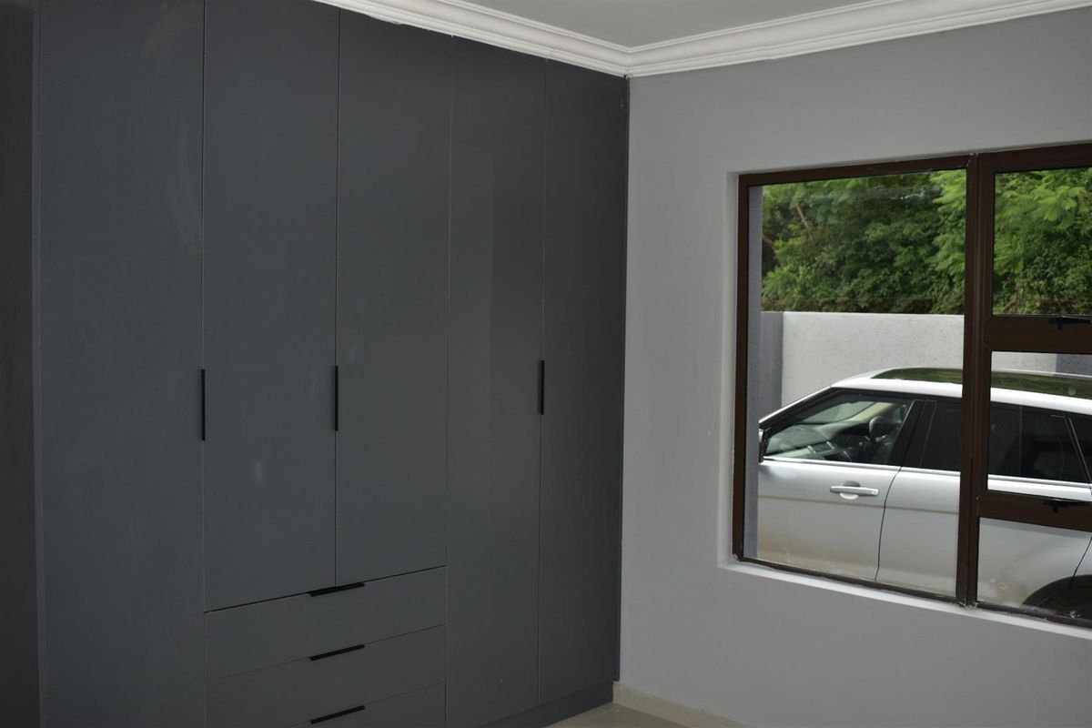 A bedroom featuring modern dark grey built-in cupboards with sleek black handles and a window overlooking the exterior.