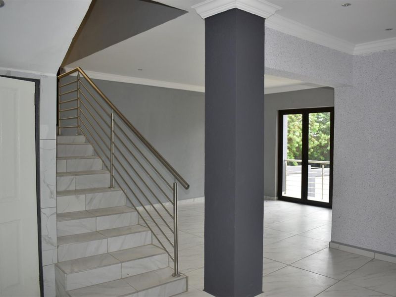 Open plan living area featuring tiled flooring, a modern staircase with stainless steel balustrades, and access to an outdoor balcony.