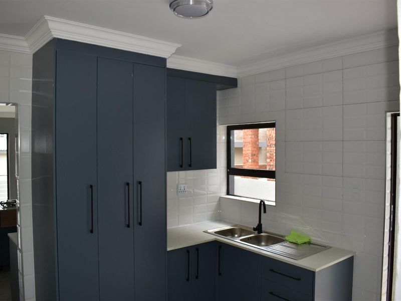 Modern scullery featuring dark blue cabinetry, white tiled backsplash, stone countertops, and a double stainless steel sink with a matte black faucet.