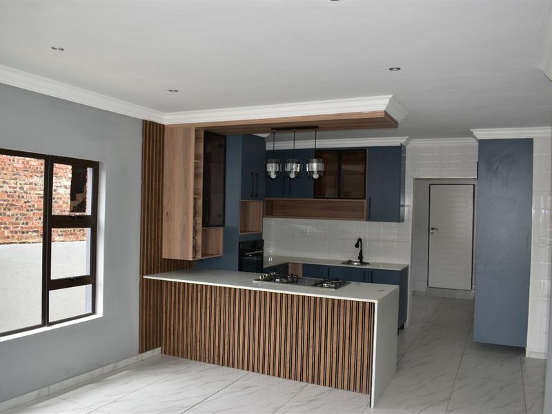 Modern open-plan kitchen featuring a central island with a built-in gas hob, sleek cabinetry, and tiled flooring.