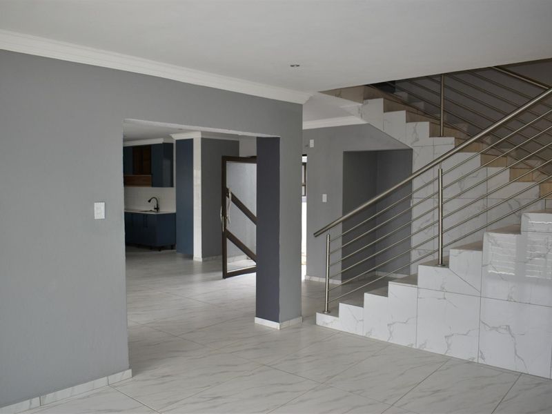 Open plan living area featuring modern marble-look floor tiles, a staircase with stainless steel balustrades, and a view through to the kitchen area.