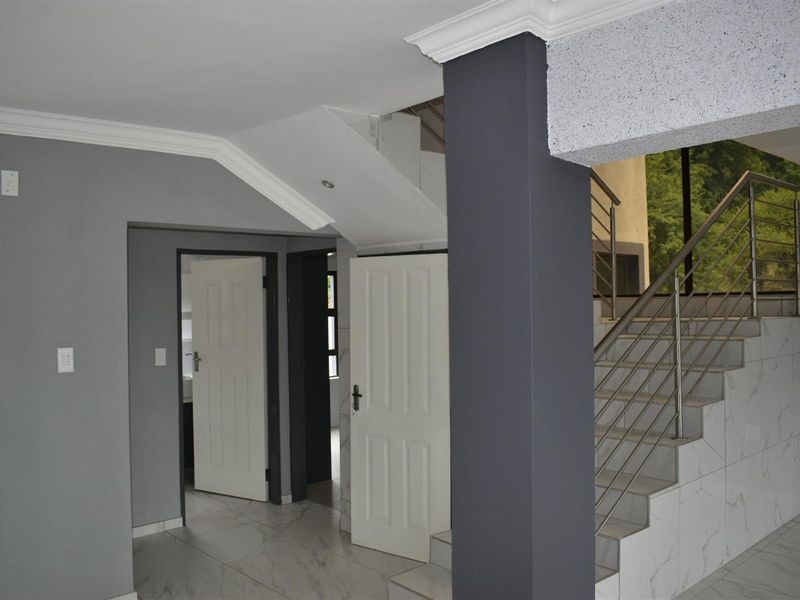 Interior view of a modern hallway featuring a tiled staircase with stainless steel balustrades, crown molding, and neutral grey wall finishes.