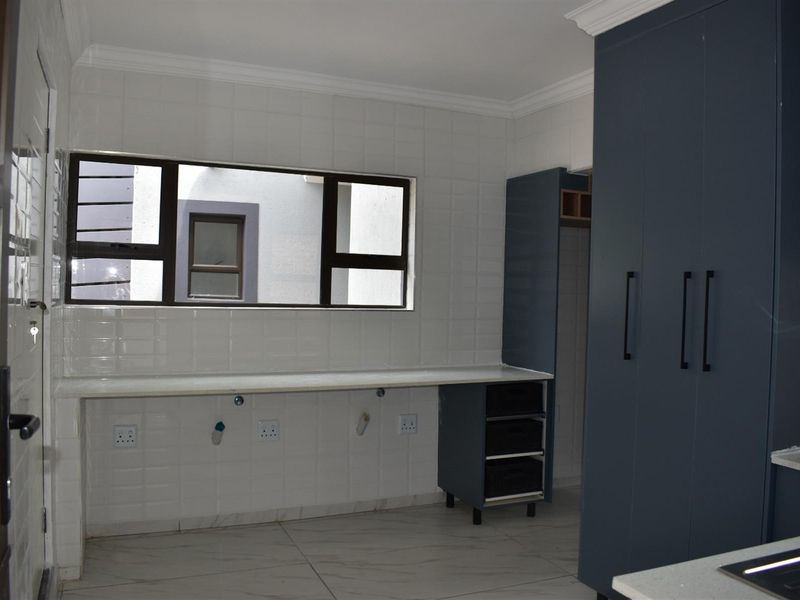 A functional scullery area featuring modern dark blue cabinetry, white tiled splashbacks, and stone-look countertops with plumbing points for appliances.