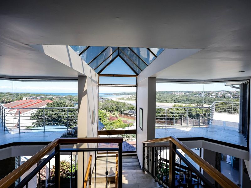 A bright, open-plan staircase area featuring a striking glass skylight, modern railings, and expansive windows offering panoramic coastal and landscape views.
