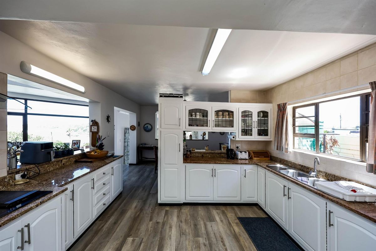 A functional kitchen featuring white cabinetry, granite countertops, a double sink, and wood-look flooring with ample natural light.