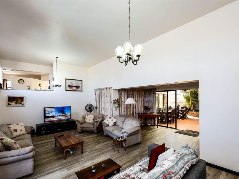 Spacious open-plan living area featuring high ceilings, wood-look flooring, and seamless flow to an outdoor patio through sliding glass doors.