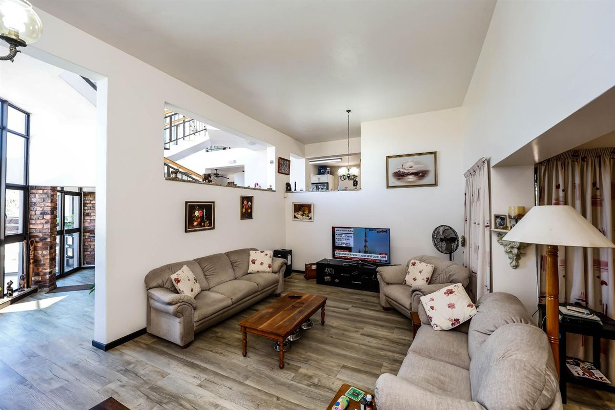 Spacious living room featuring wood-look laminate flooring, high ceilings, and an open-plan design with a view into the adjacent hallway and staircase area.