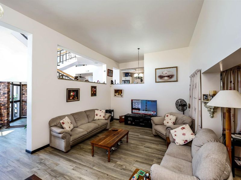 Spacious living room featuring wood-look laminate flooring, high ceilings, and an open-plan design with a view into the adjacent hallway and staircase area.