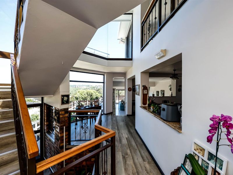 A bright, multi-level hallway featuring a staircase with metal railings, wood-look flooring, and an open-plan layout connecting to adjacent living spaces.