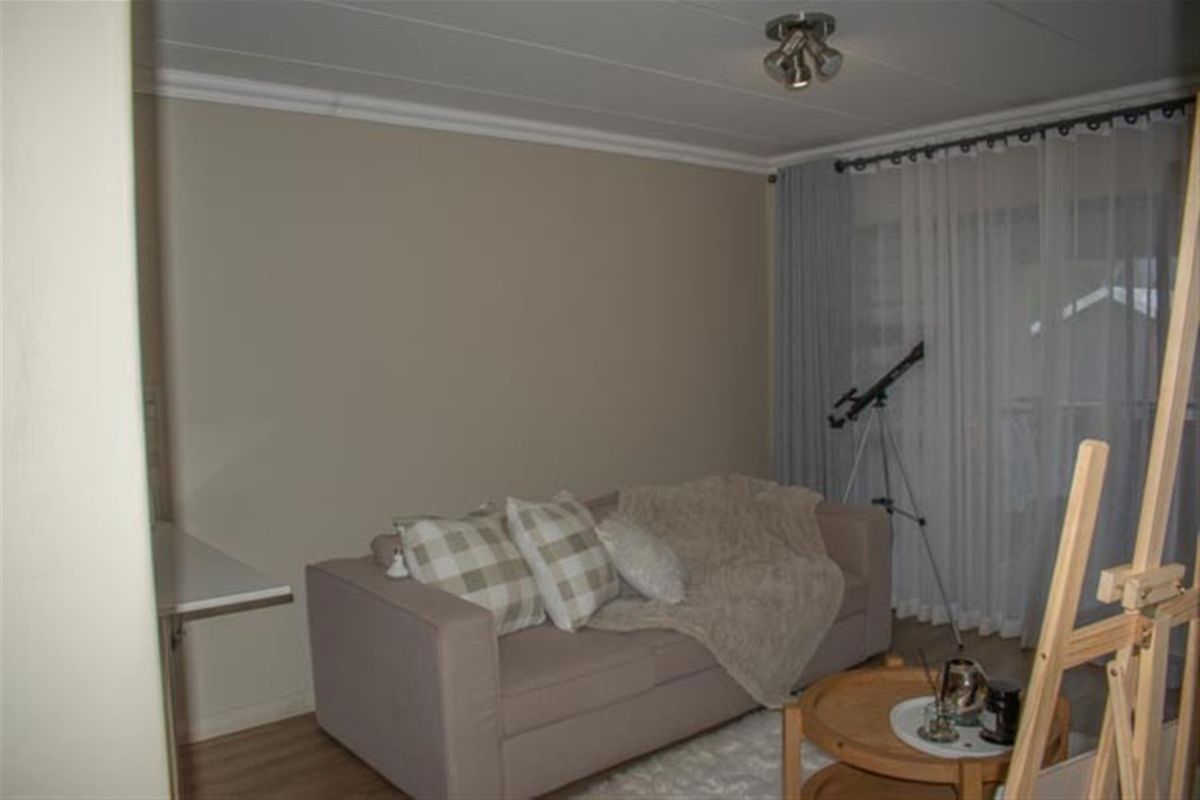 A living room featuring neutral wall tones, laminate flooring, and a sliding door with sheer curtains leading to an outdoor area.