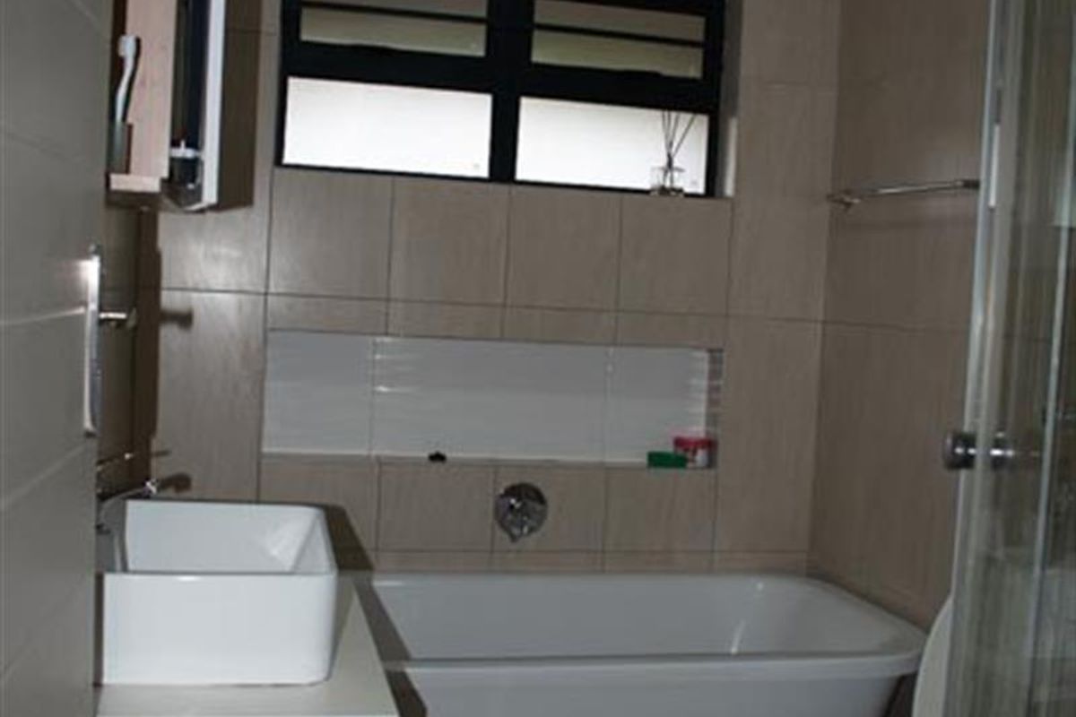 A functional bathroom featuring a bathtub, a modern vessel sink vanity, a toilet, and a glass-enclosed shower area with neutral wall tiling.