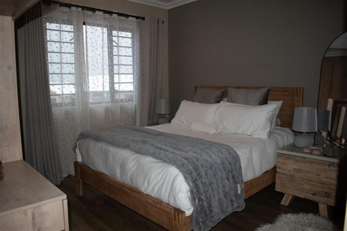 A well-maintained bedroom featuring neutral wall tones, wood-look flooring, and a large window that allows for natural light.