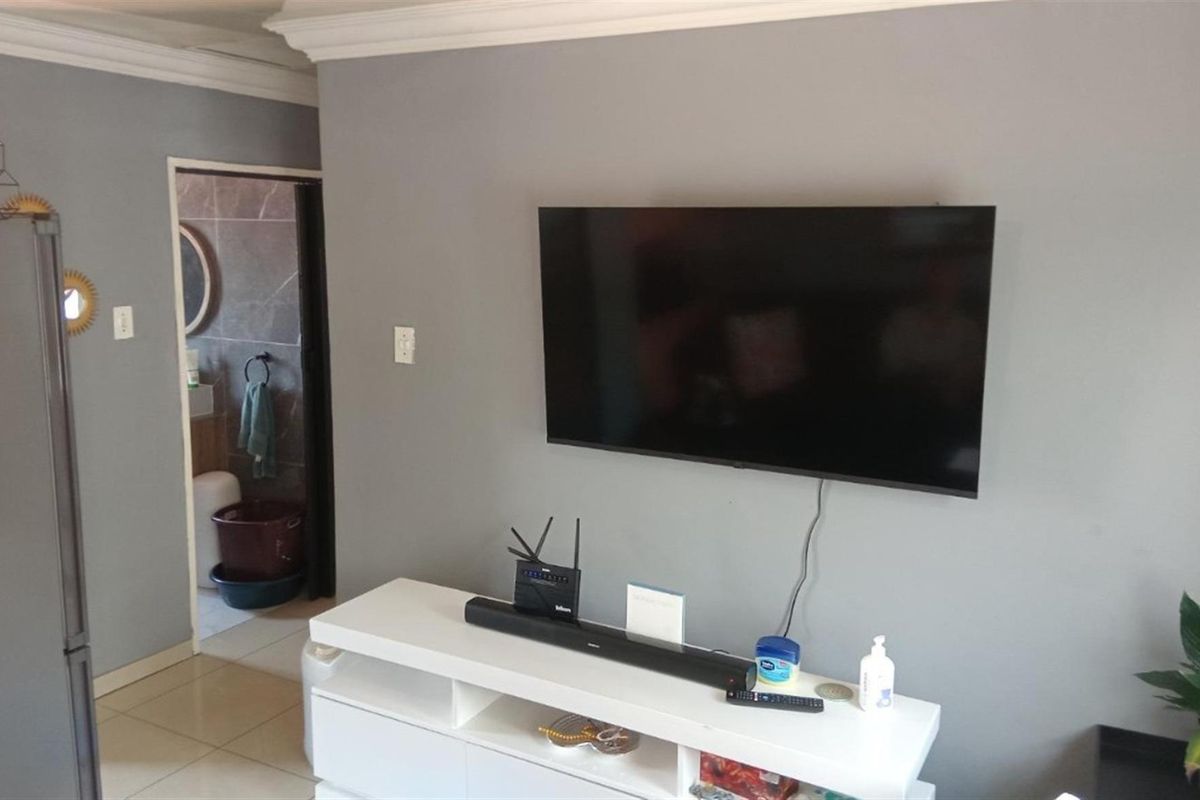 A view of a living area featuring grey walls, crown molding, and tiled flooring, with a direct view into an adjacent bathroom.