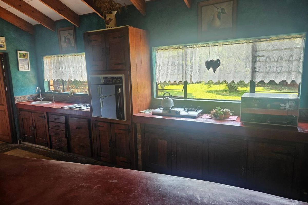 A rustic kitchen featuring dark timber cabinetry, exposed wooden ceiling beams, and integrated cooking appliances with views over the garden.