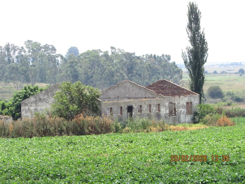 A dilapidated farm building structure showing significant deterioration and missing roof elements, situated within a rural agricultural landscape.