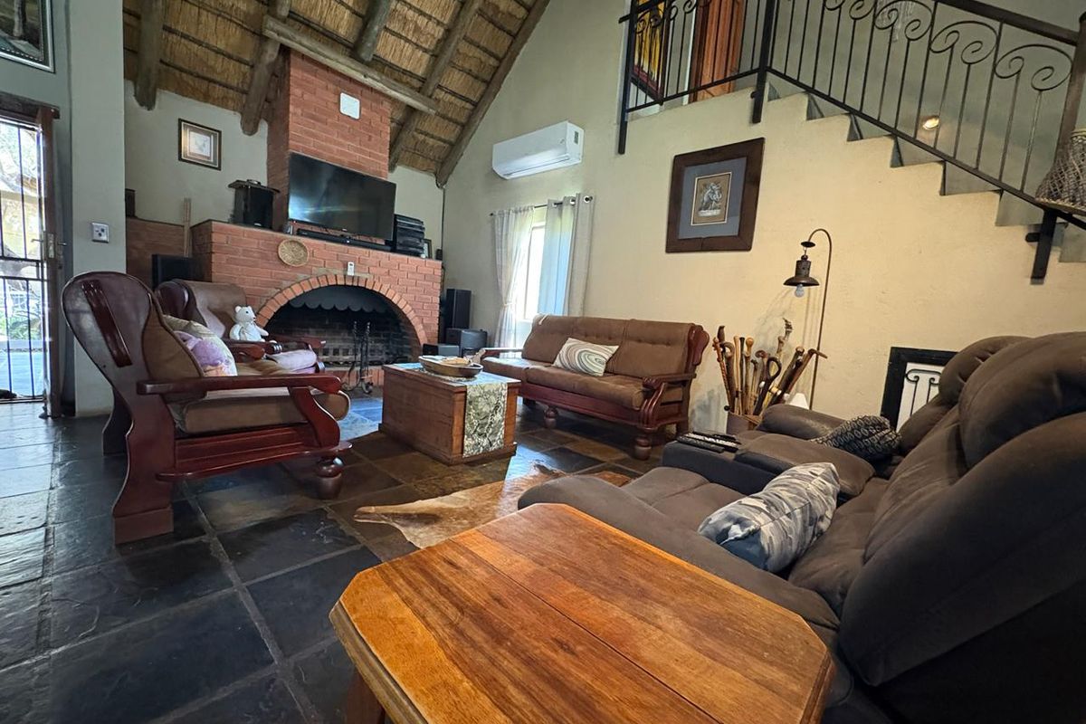 Spacious living room featuring a high thatched ceiling with exposed rafters, a prominent brick fireplace, slate flooring, and an internal staircase with iron railing.