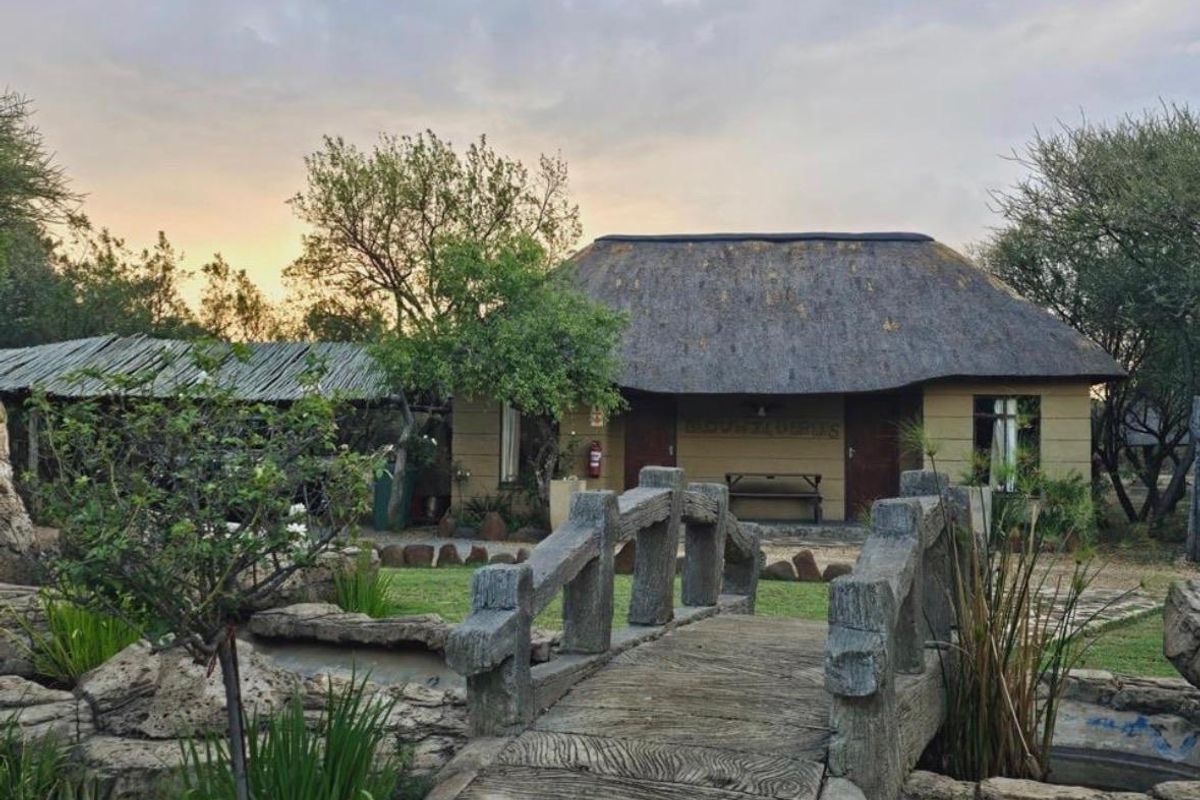 A charming farm-style dwelling featuring a traditional thatch roof, a decorative stone bridge, and a well-maintained garden setting.