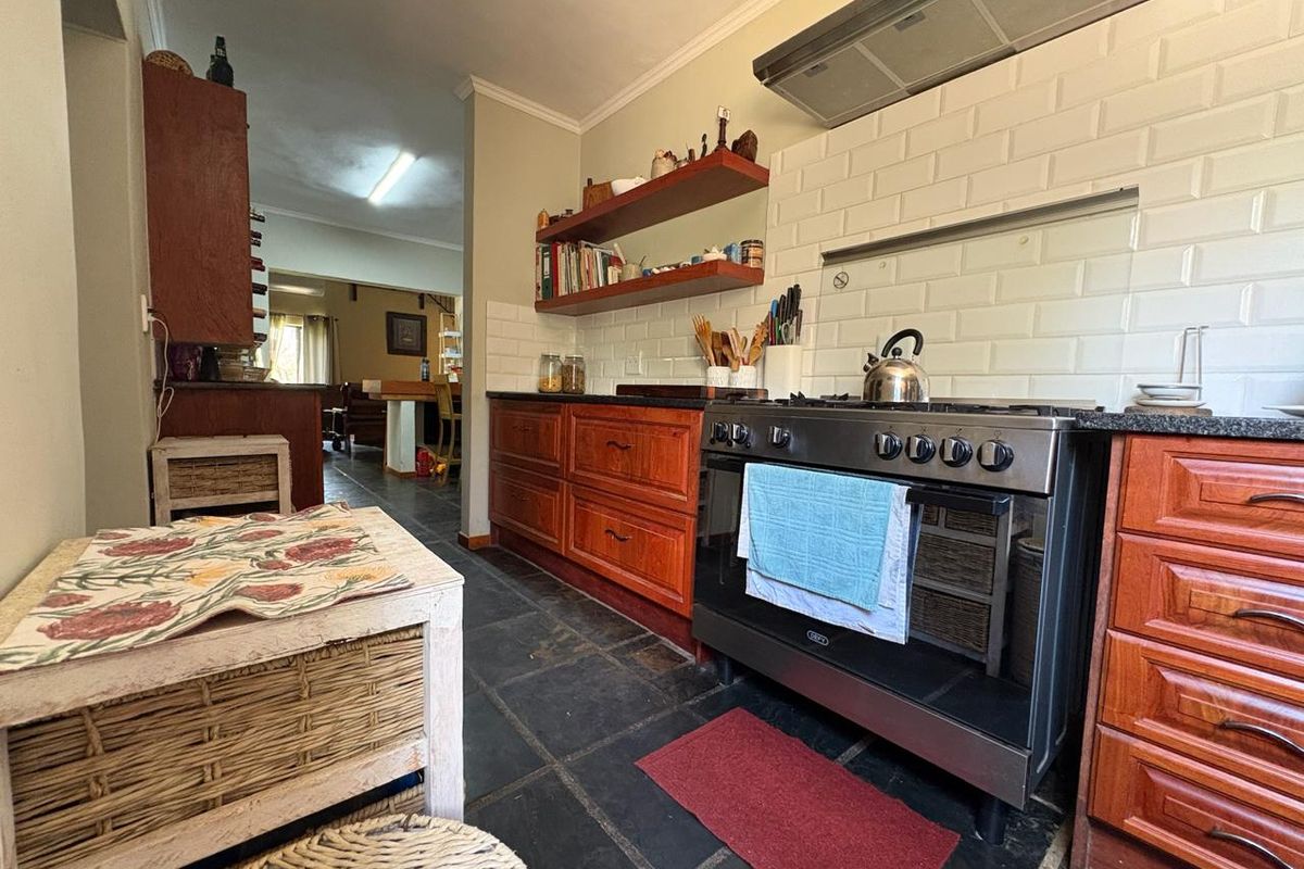 A rustic kitchen featuring wooden cabinetry, a gas stove with extractor fan, subway tile backsplash, and dark slate flooring.