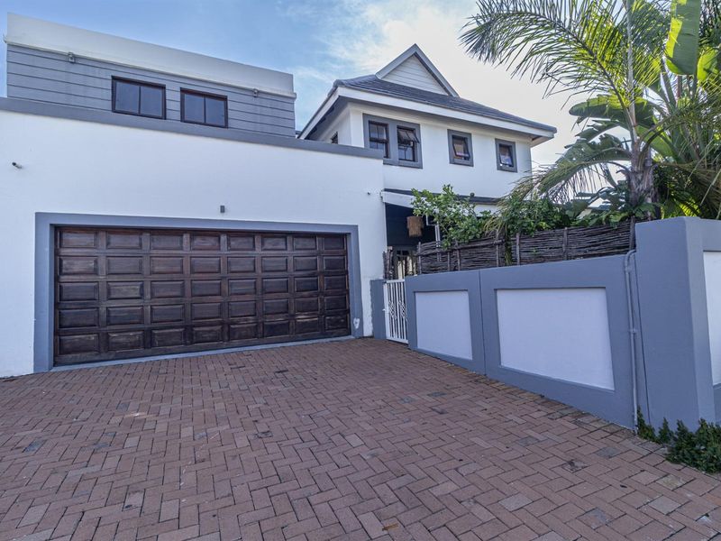 Front elevation of the property featuring a paved driveway, double garage, and secure boundary wall with pedestrian access.