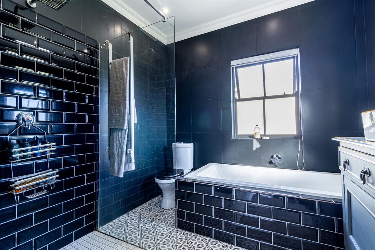 Modern bathroom featuring striking black subway wall tiles, patterned floor tiling, a built-in bathtub, and a glass-enclosed shower area.