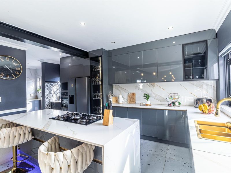 Modern, high-end kitchen featuring glossy grey cabinetry, marble-look stone countertops, a central island with a gas cooktop, and premium gold-finish fixtures.