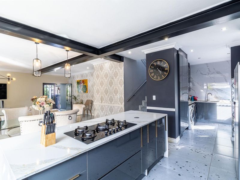 Modern open-plan living area featuring a sleek kitchen with stone-topped island, gas hob, and contemporary finishes, seamlessly flowing into the dining and lounge space.