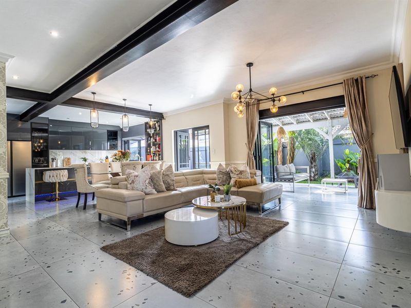 Spacious open-plan living area featuring modern kitchen with island, exposed steel beams, and seamless flow to a covered patio through large bi-fold doors.