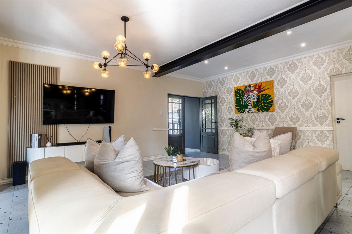 A well-maintained living room featuring a striking exposed steel beam, decorative wallpaper, slatted wood accents, and modern lighting fixtures.