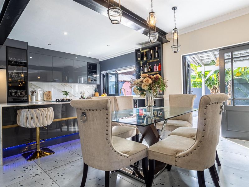 Modern open-plan kitchen and dining area featuring high-gloss cabinetry, a stone island, exposed ceiling beams, and seamless access to the outdoor patio.