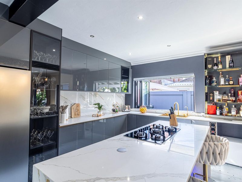 Modern kitchen featuring high-gloss grey cabinetry, marble-look stone countertops, a central island with a gas hob, and elegant brass fixtures.