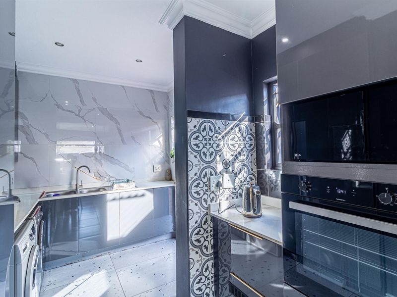 Modern kitchen featuring high-gloss cabinetry, stone countertops, marble-look splashbacks, and integrated appliances including a built-in oven and microwave.