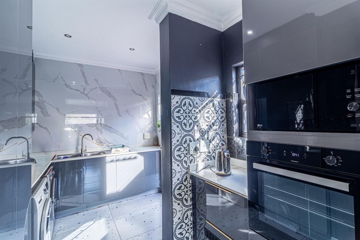 Modern kitchen featuring high-gloss cabinetry, stone countertops, marble-look splashbacks, and integrated appliances including a built-in oven and microwave.