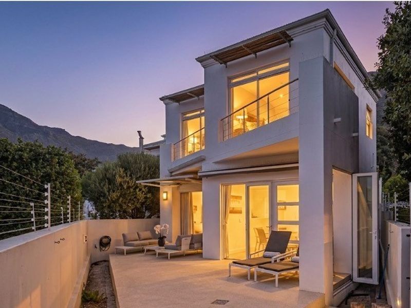 Rear view of a modern two-story townhouse featuring a paved patio, upper-level balcony, and secure perimeter fencing at dusk.