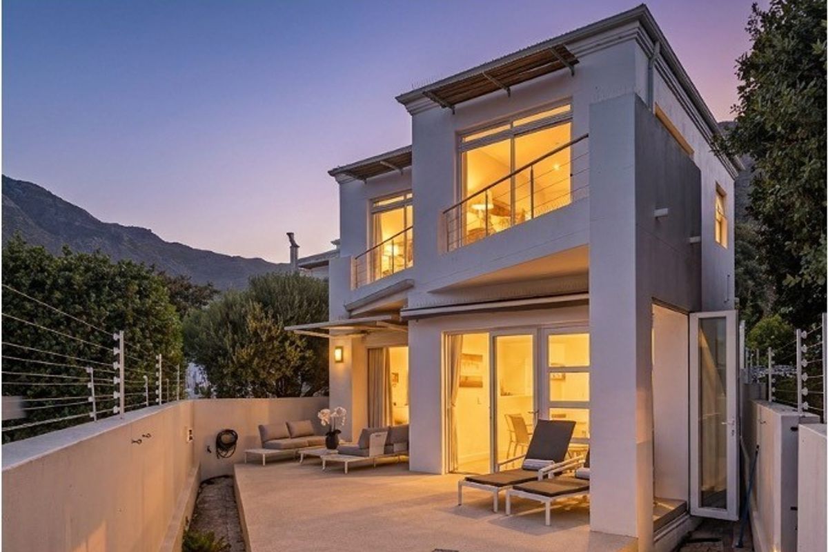Rear view of a modern two-story townhouse featuring a paved patio, upper-level balcony, and secure perimeter fencing at dusk.