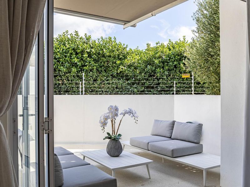 A private covered patio area featuring a retractable awning, paved flooring, and secure perimeter fencing with established greenery.