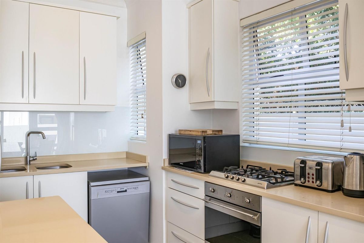 A well-maintained kitchen featuring white cabinetry, stone countertops, a gas cooktop, built-in oven, and a stainless steel sink with a glass splashback.