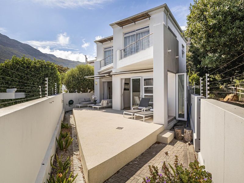 Rear view of a modern townhouse featuring a paved patio area, upper-level balcony, and secure perimeter with electric fencing.