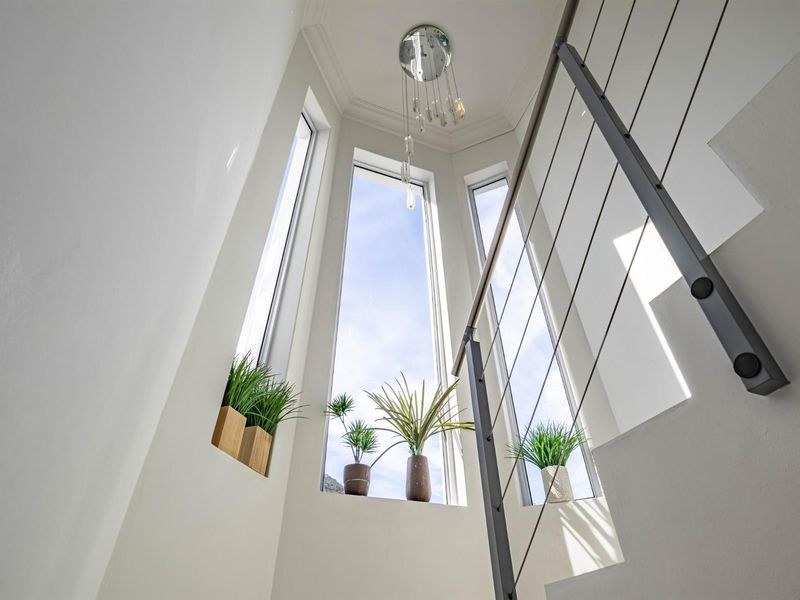 A bright, modern stairwell featuring a sleek metal balustrade and tall, full-height windows that provide ample natural light.