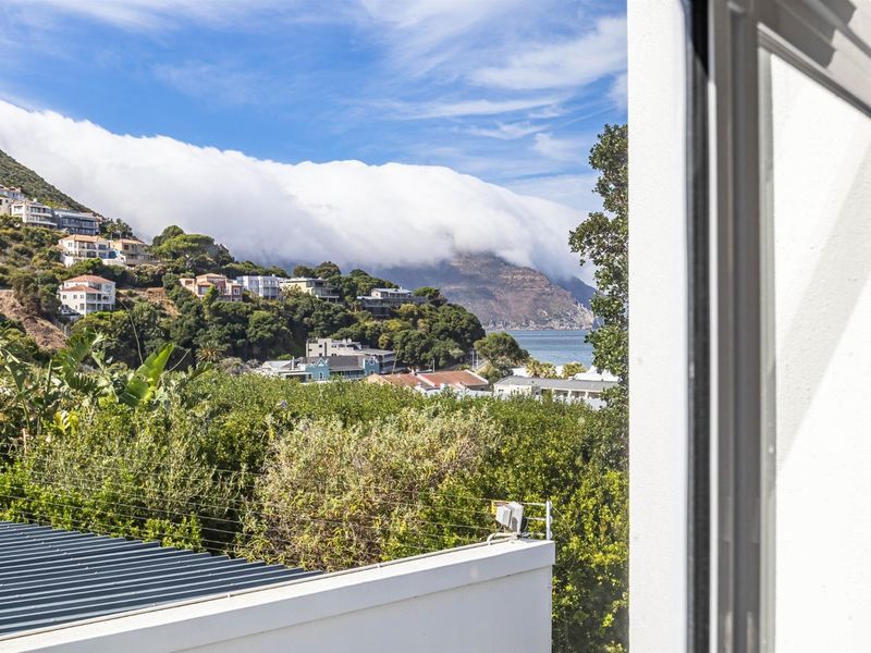 A scenic elevated view overlooking the coastal landscape, hillside residential area, and ocean, framed from an interior window.