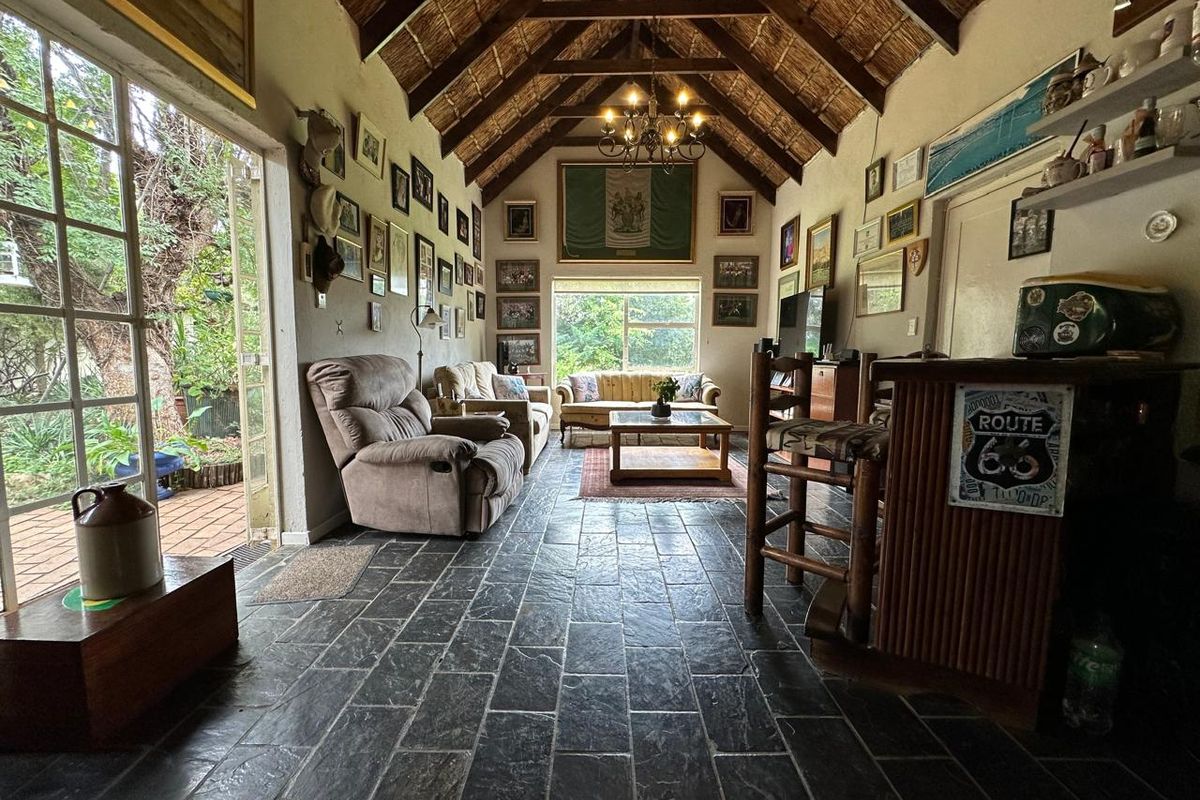 Spacious living room featuring a high vaulted thatched ceiling with exposed timber trusses, slate tile flooring, and direct access to the garden via french doors.