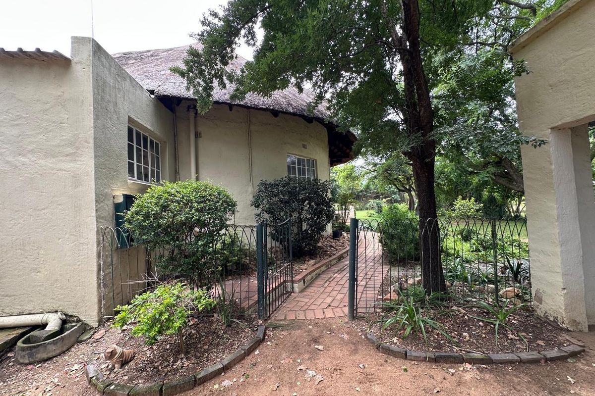 A rear exterior view of a farm-style property featuring a thatched roof, brick pathways, and established garden landscaping.