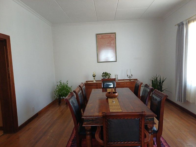A formal dining room featuring polished timber flooring, neutral walls, and a large window with curtain treatments.