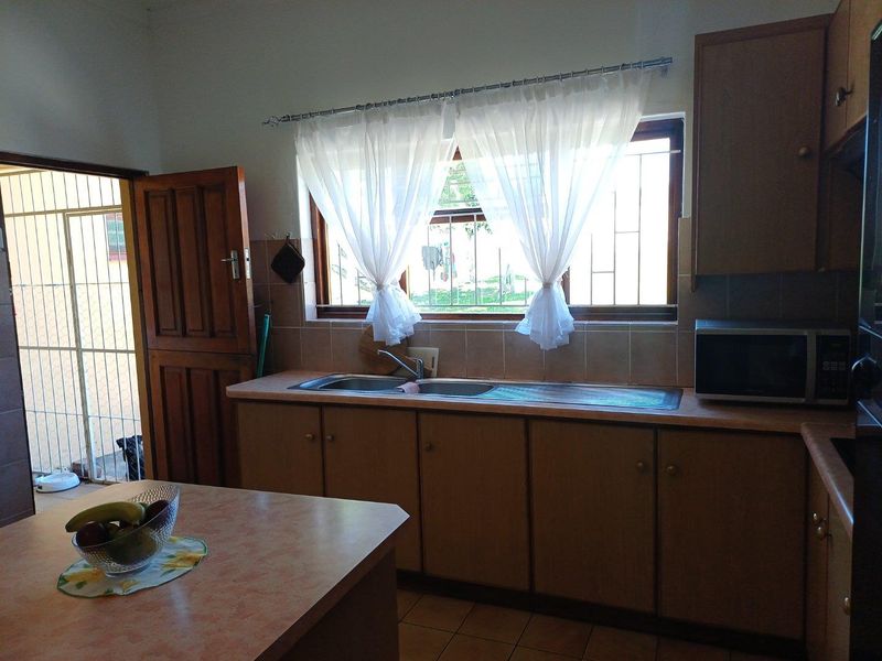 A functional kitchen featuring wooden cabinetry, a double-basin stainless steel sink, tiled splashbacks, and direct access to an exterior area.