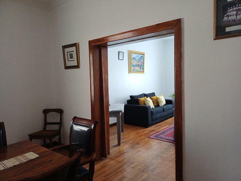 A view through a wooden doorway connecting a dining area to a living room, featuring polished timber flooring and neutral wall finishes.