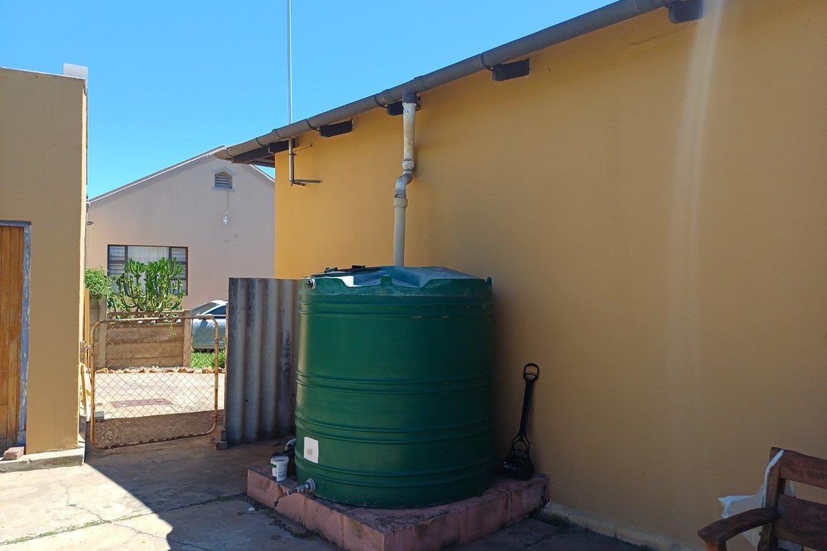 Exterior view of the property rear featuring a large green water storage tank connected to the roof gutter system on a concrete base.